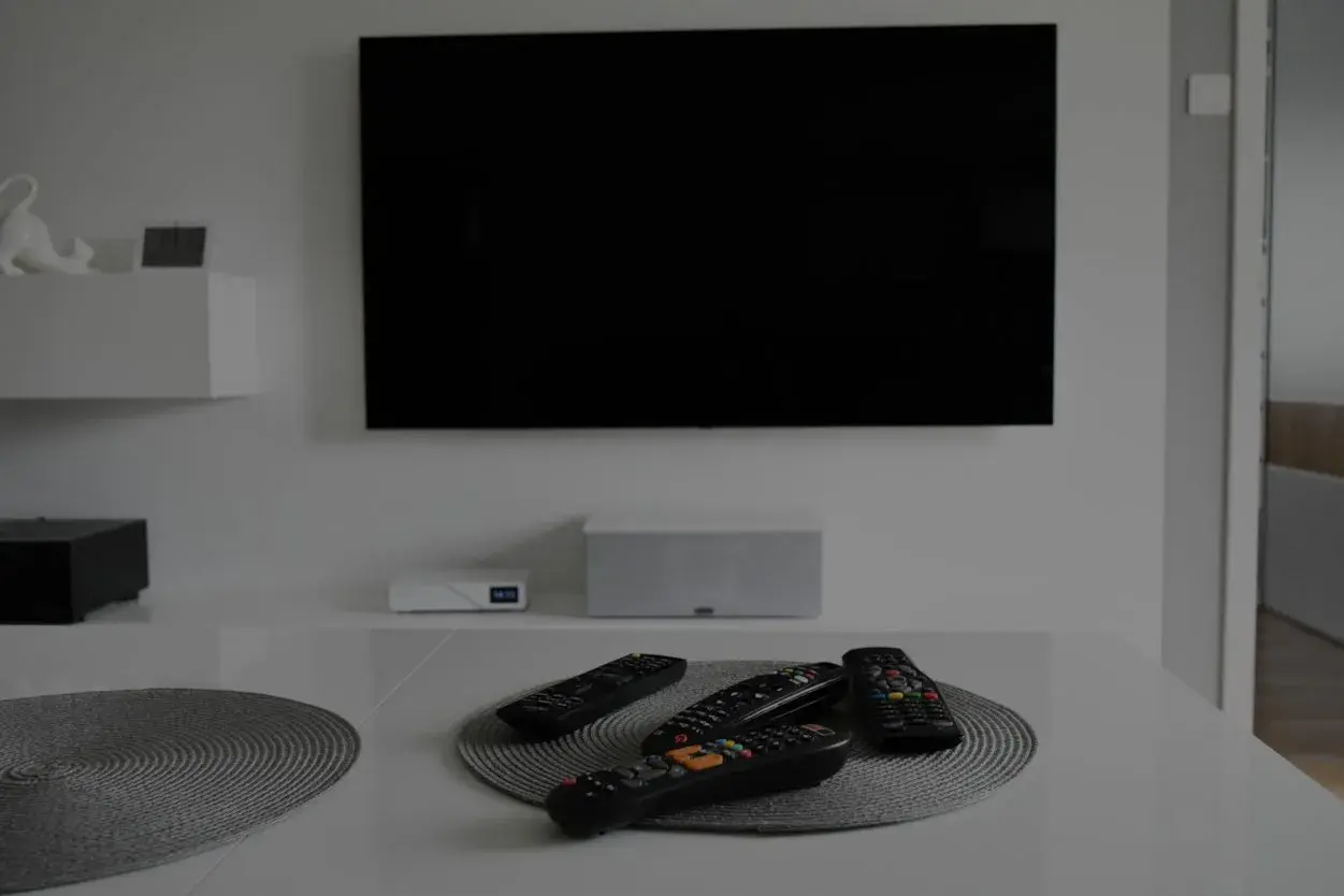 Na stole leżą piloty, a czarny ekran telewizora sugeruje, że jest brak obrazu w telewizorze.