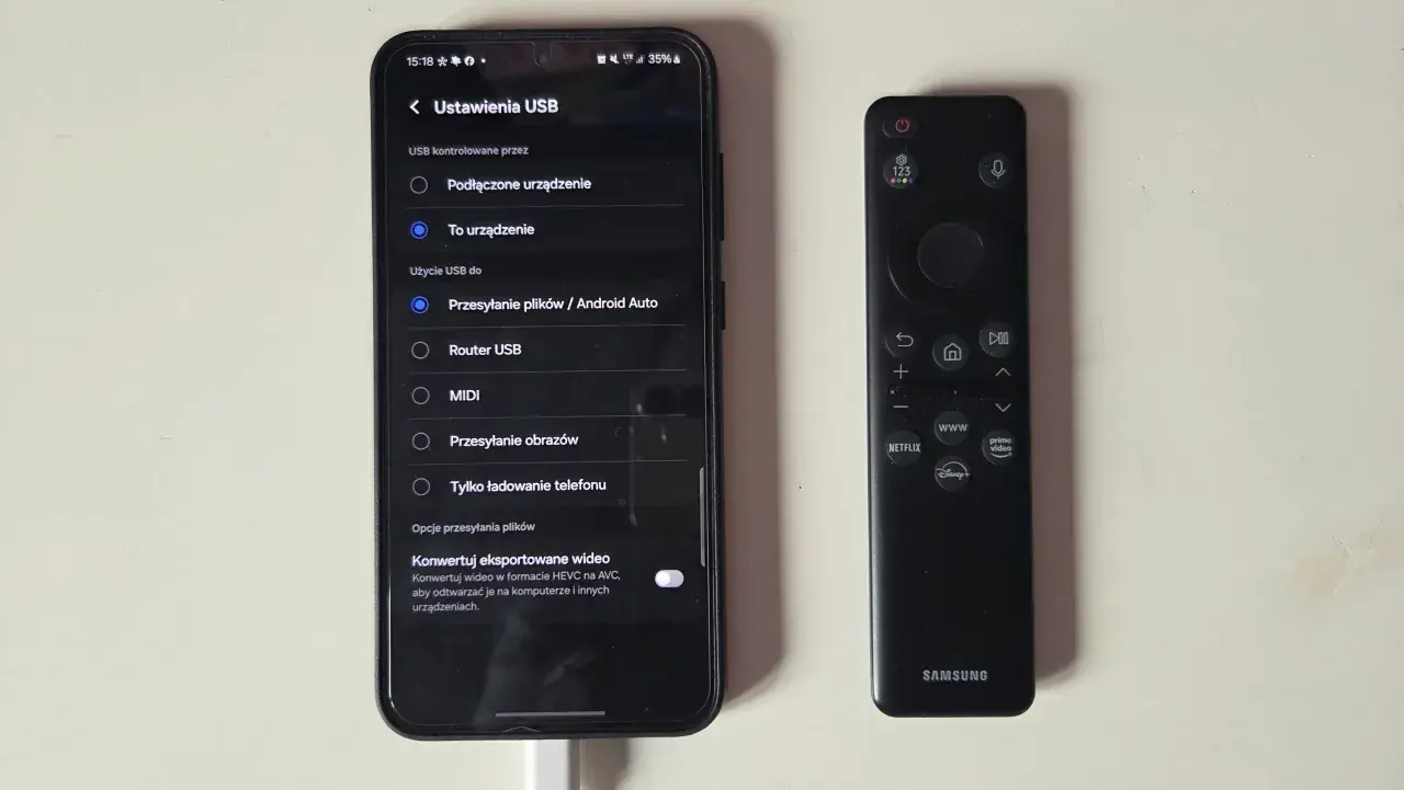 Telefon z włączonym klonowaniem ekranu obok pilota Samsunga. Ustawienia USB pokazują opcję "Przesyłanie plików / Android Auto".