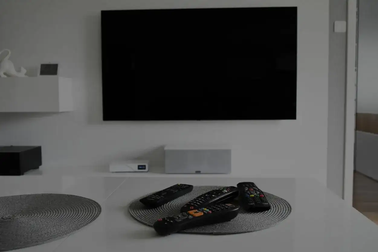 Na stole leżą piloty, a czarny ekran telewizora sugeruje, że jest brak obrazu w telewizorze.