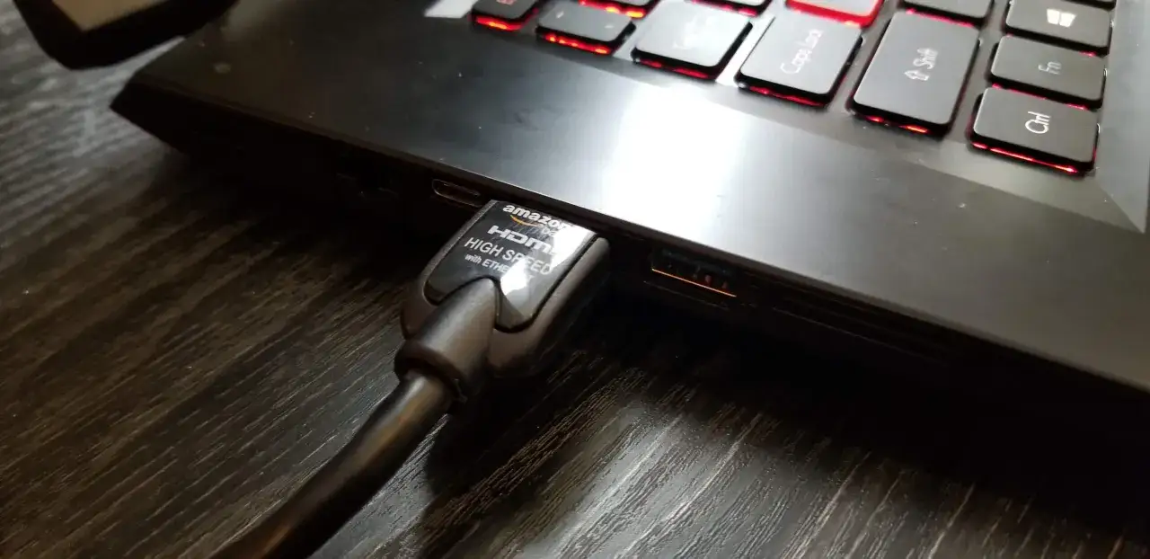 Kabel HDMI podłączony do laptopa, gotowy do klonowania ekranu. Podświetlana klawiatura dodaje klimatu.