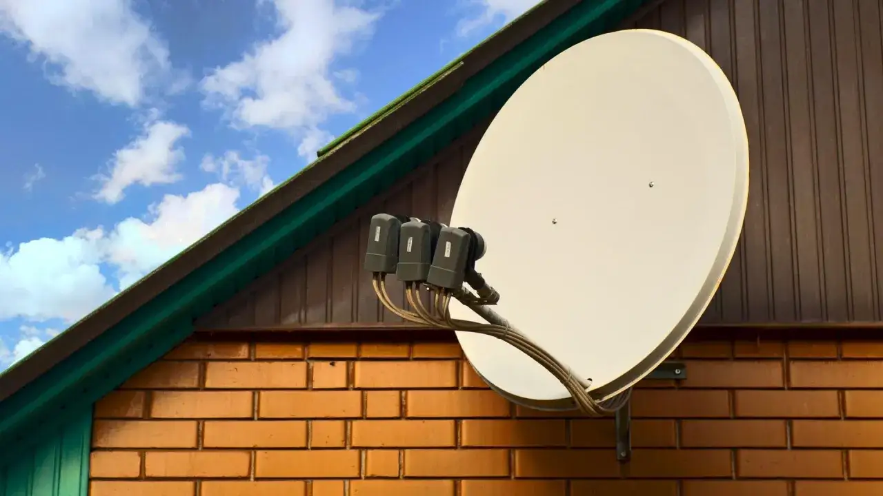 Talerz anteny satelitarnej zamontowany na ceglanej ścianie domu, gotowy do odbioru sygnału tv satelitarnej.